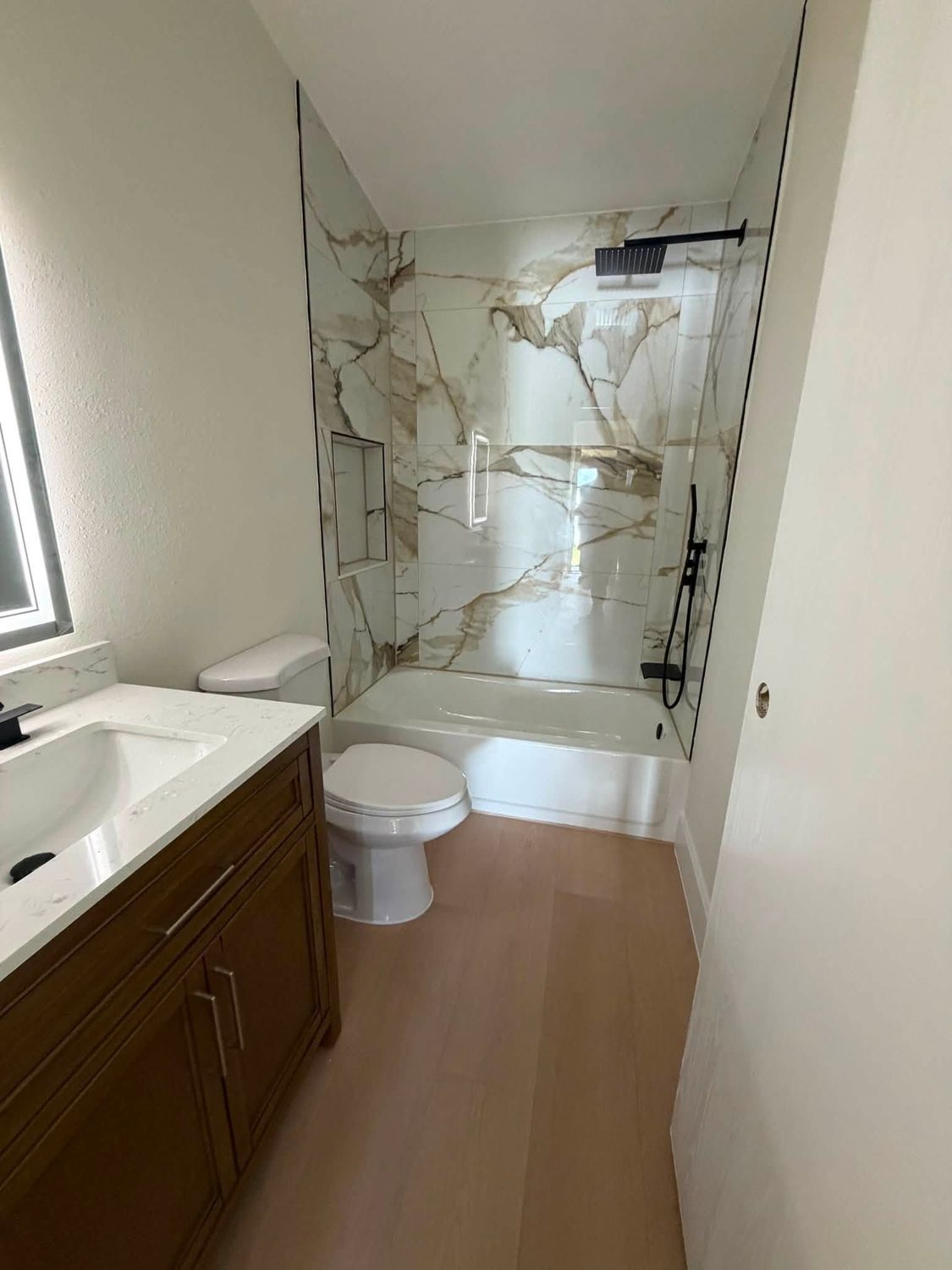 The same guest bathroom after remodeling, with a tiled tub surround, quartz vanity top and new plank flooring