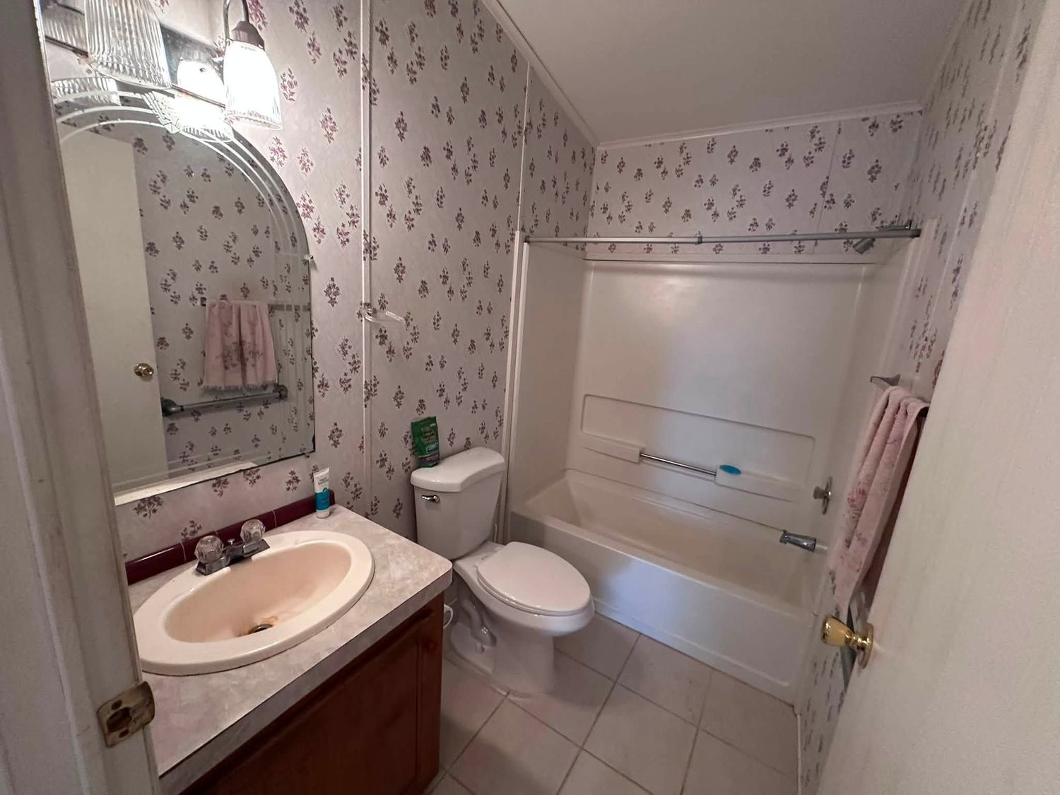 Guest bathroom before remodeling, with floral wallpaper, an oak vanity and a dated tub