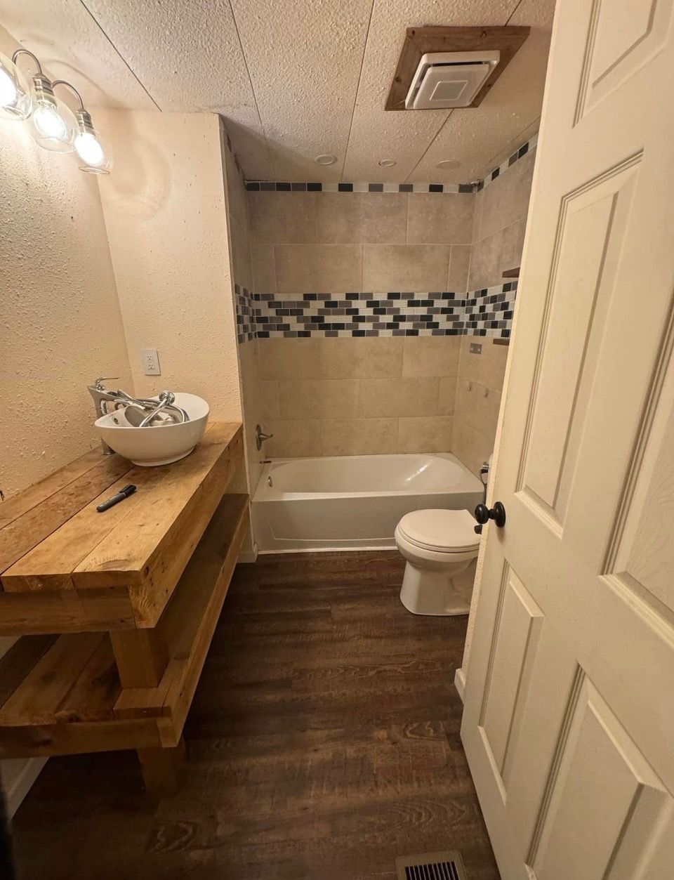Bathroom before remodeling, with a reclaimed timber vanity, tan tile tub surround and mosaic accent band