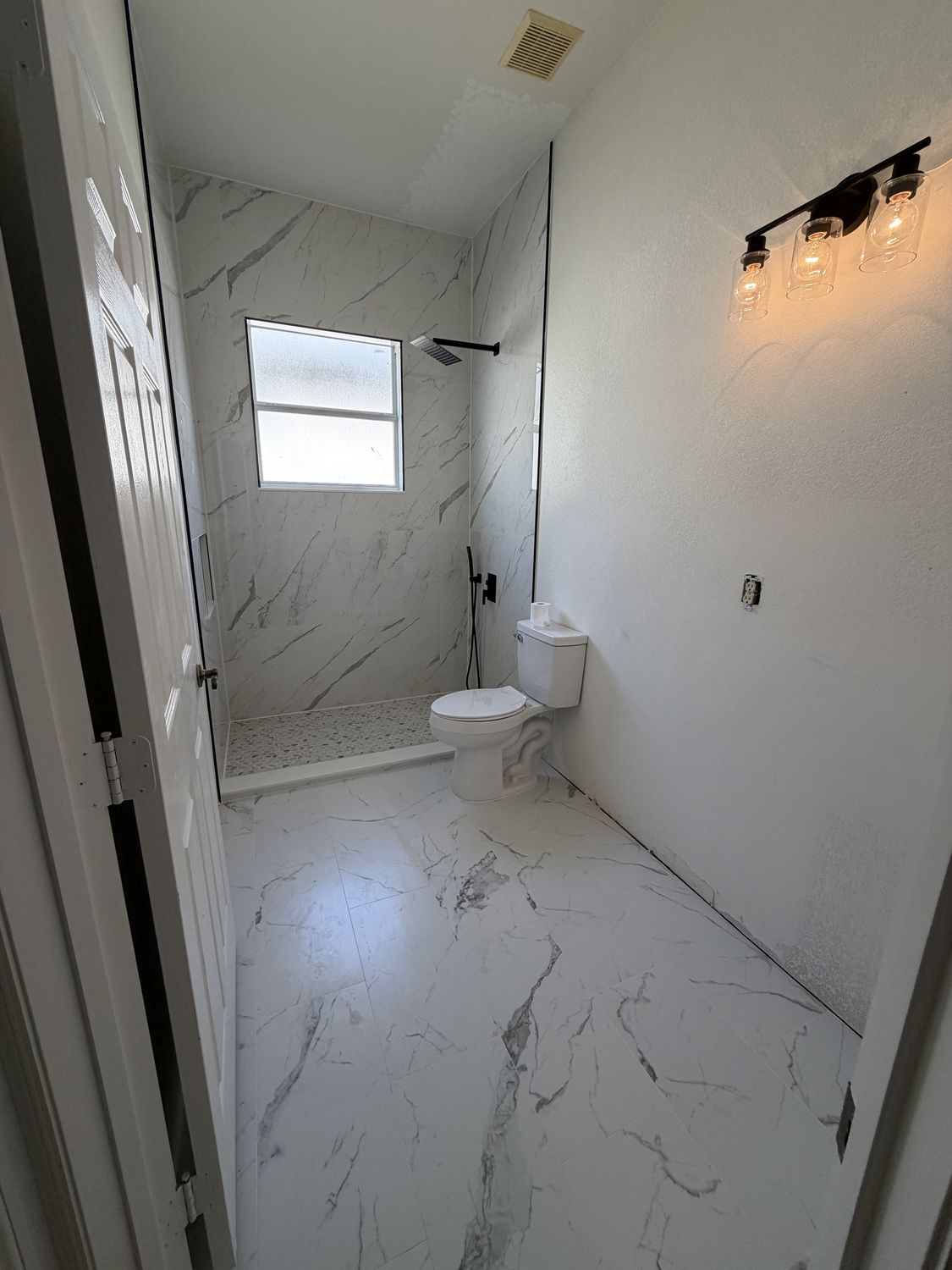 The same bathroom after remodeling, with the tub replaced by a curbless walk-in shower in marble-look porcelain, matte black fixtures and large-format floor tile