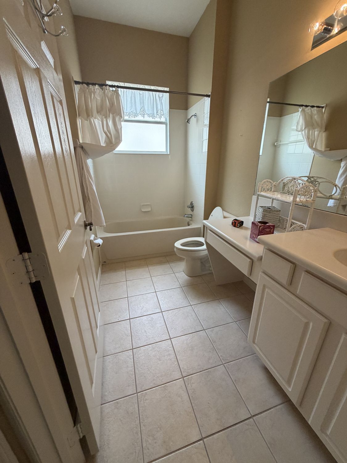 Bathroom before remodeling, with a builder tub behind a shower curtain, a cultured-marble vanity and beige floor tile