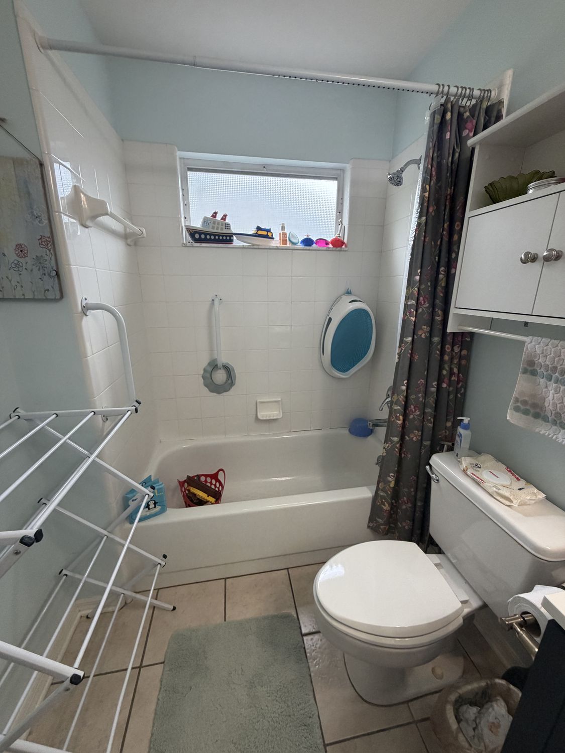 Family bathroom before remodeling, with a white square-tile tub surround, shower curtain and pale blue walls