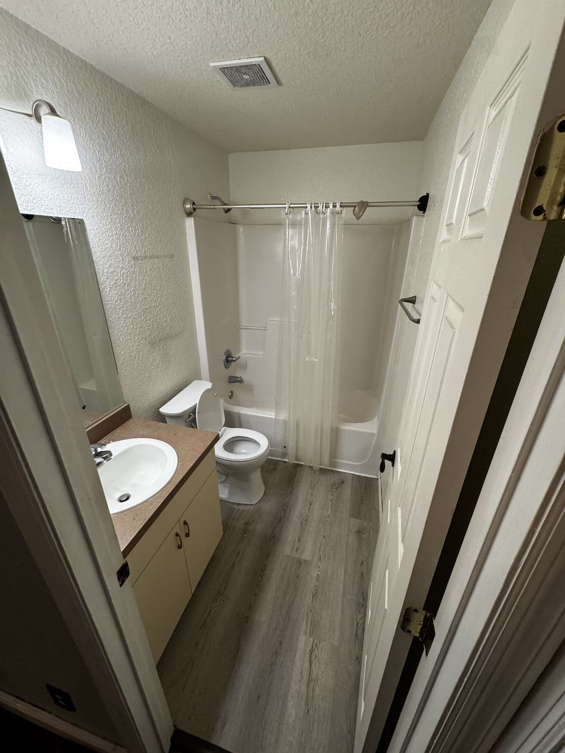 Bathroom before remodeling, with a builder-grade vanity and a fiberglass tub behind a shower curtain