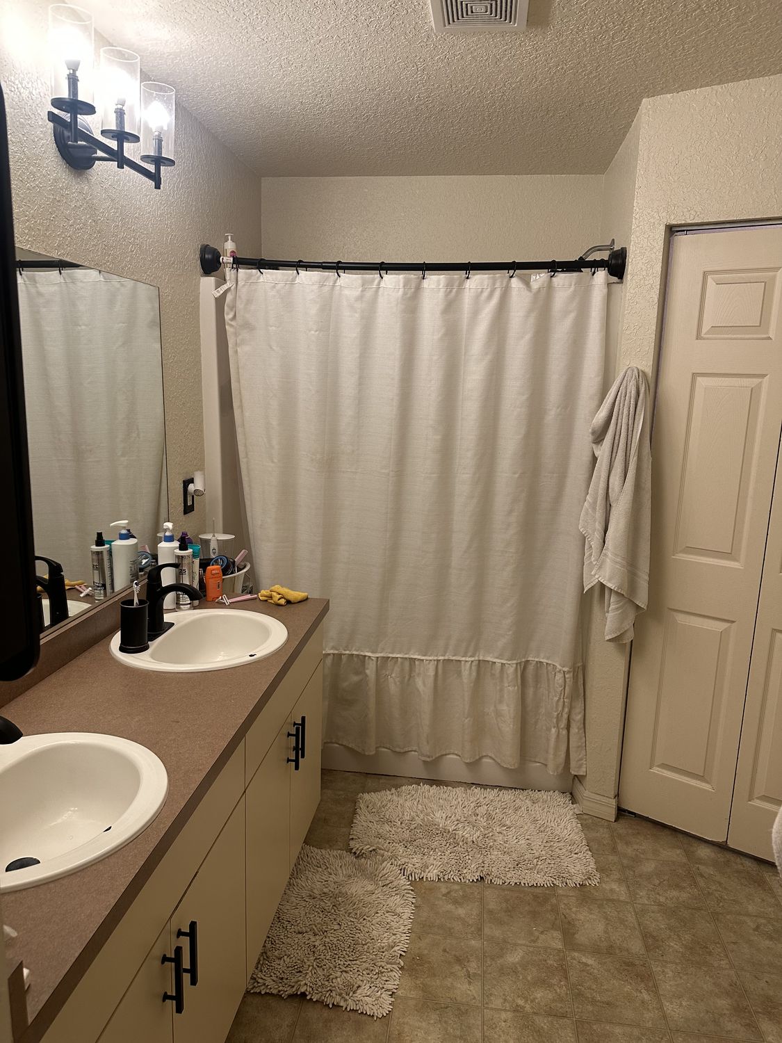 Bathroom before remodeling, with a laminate-topped double vanity and a tub behind a shower curtain