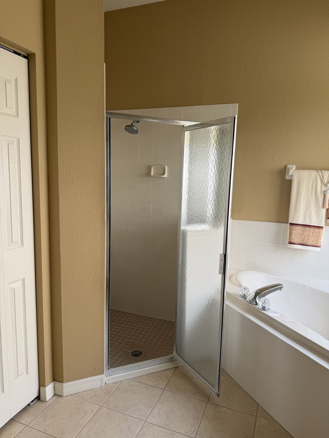 Master bathroom before remodeling, with gold walls, a framed frosted-glass shower enclosure and a beige tile floor beside a garden tub