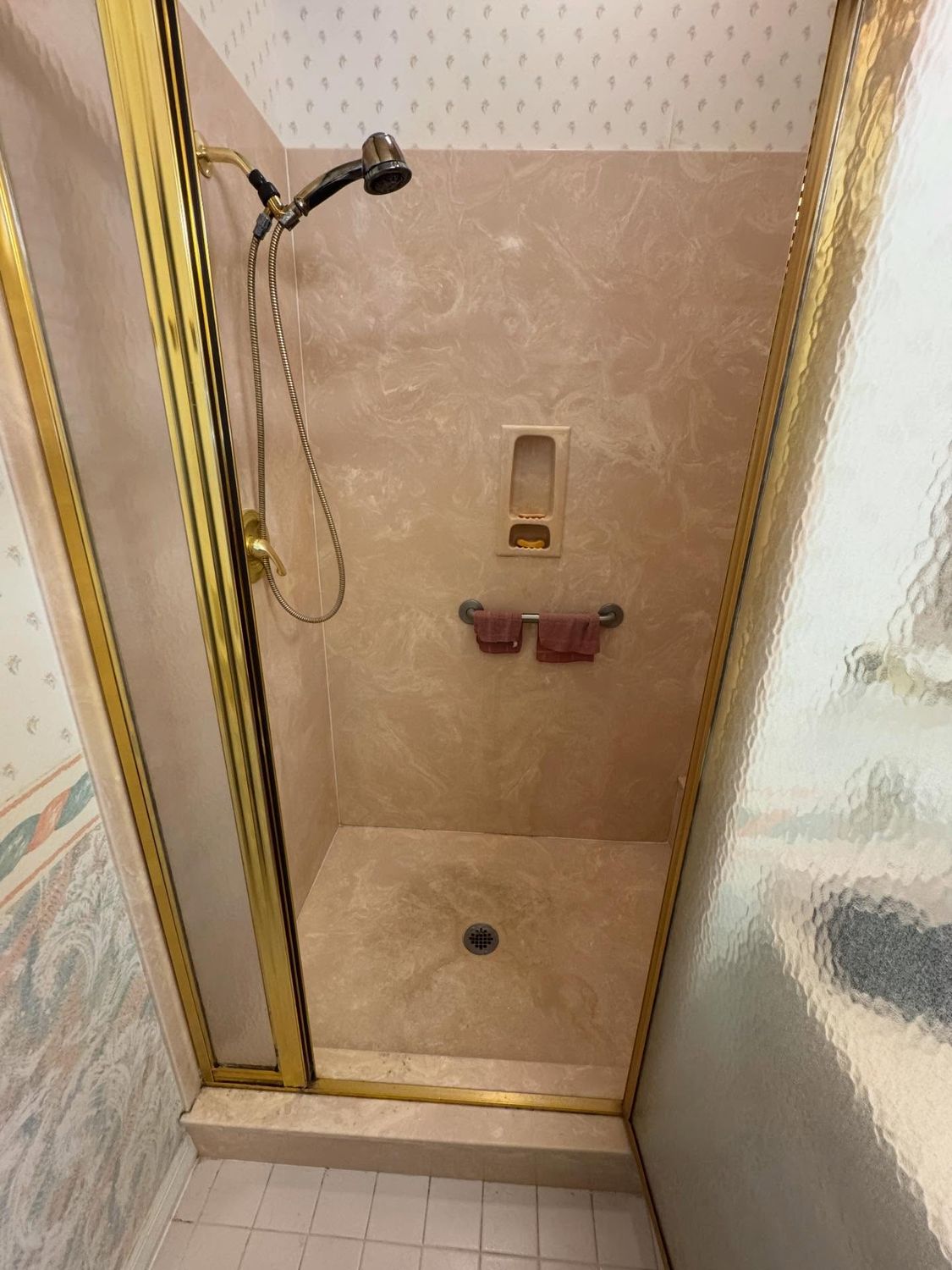 Master shower before remodeling, a small enclosure with a gold-framed door and pink cultured marble