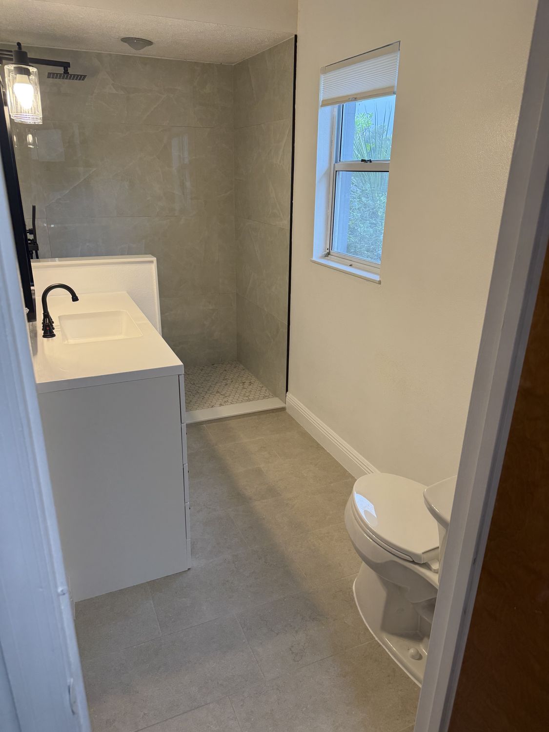 The same bathroom after remodeling, with an open walk-in shower in large-format porcelain, a new white vanity and new tile flooring