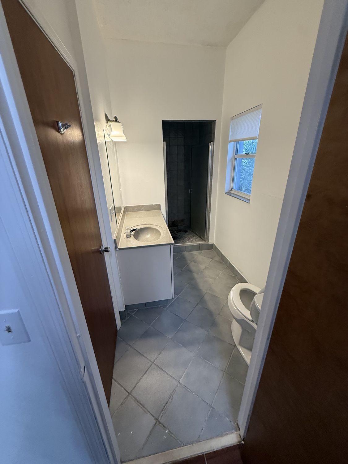 Bathroom before remodeling, seen through the doorway, with a dark enclosed shower stall at the back