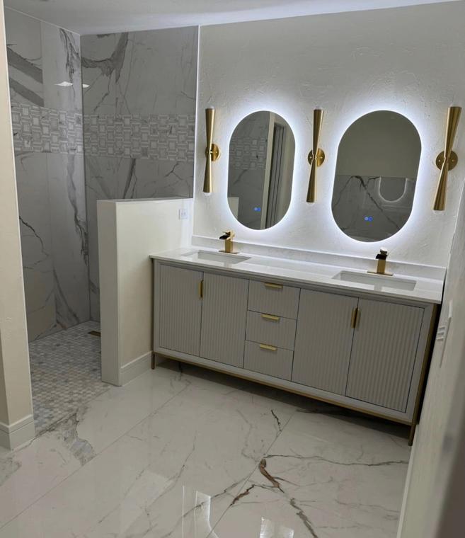 Double vanity with fluted cabinetry, brass fixtures and backlit mirrors