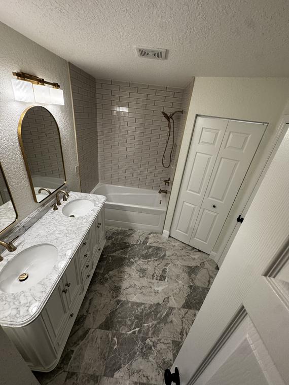 Marble-topped double vanity, arched mirror and subway-tile tub