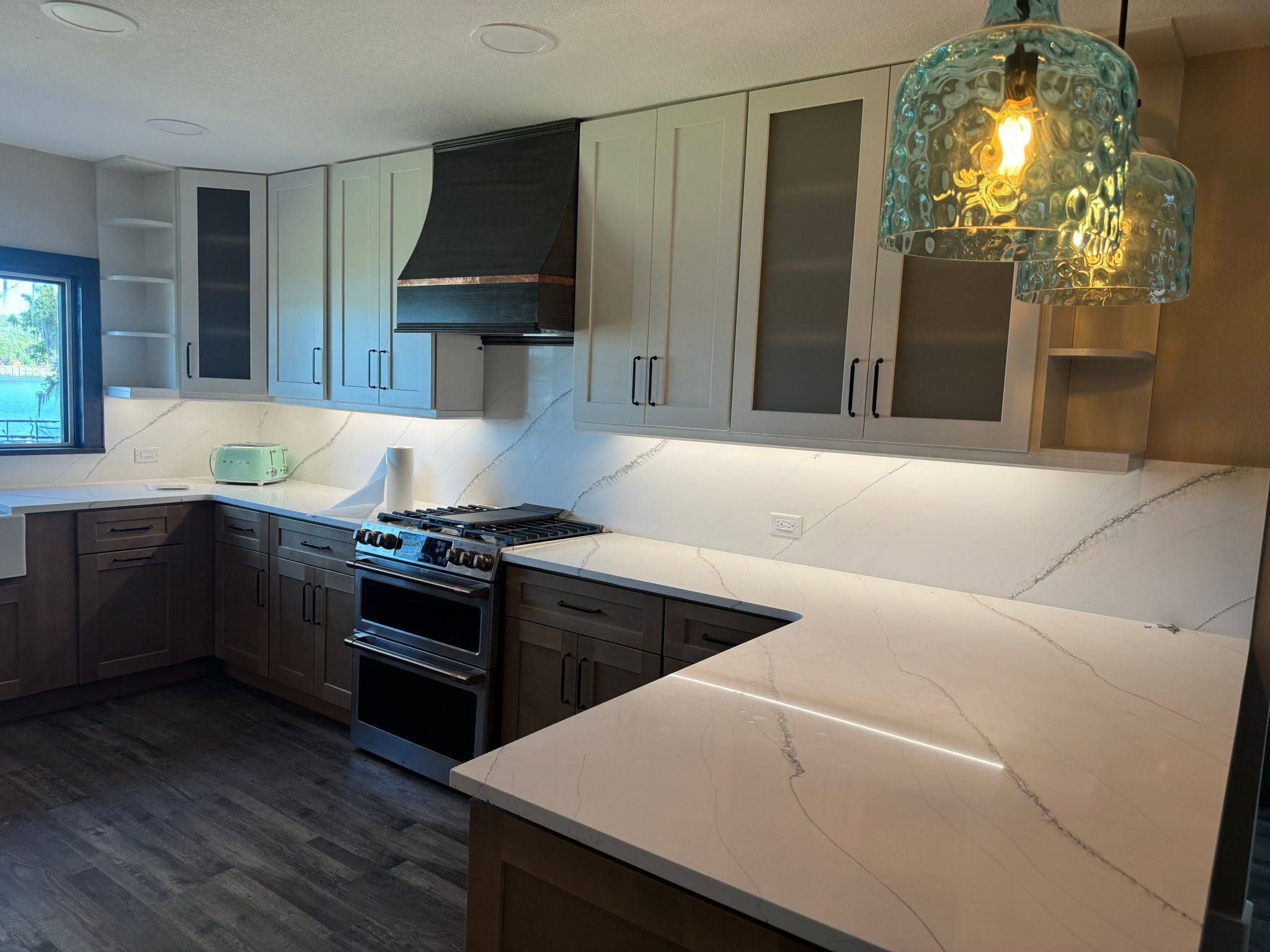 Remodeled kitchen with two-tone cabinetry, waterfall quartz counters and a custom range hood