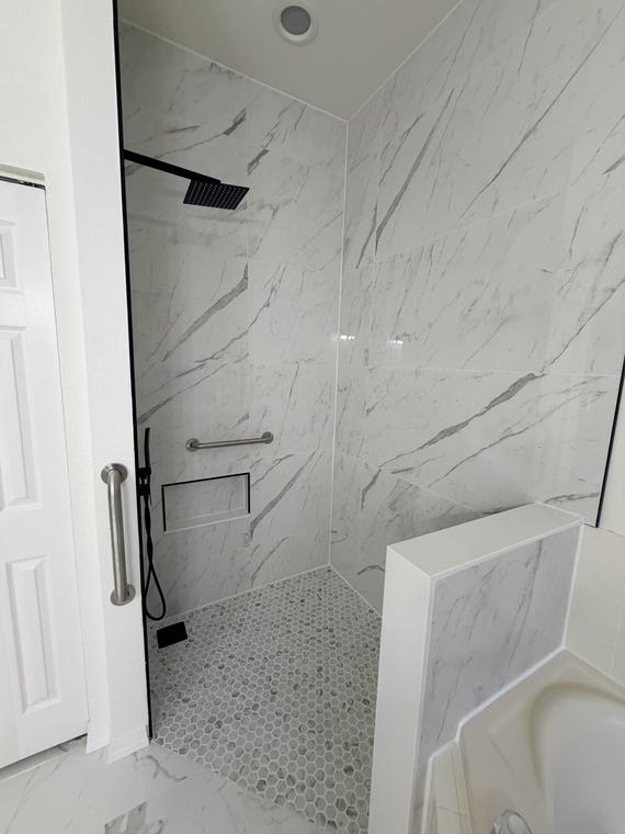 After — inside the finished shower: pebble floor, tile bench and matte black fixtures